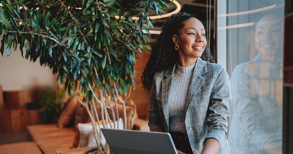 Empleada con su computadora portátil en su oficina mirando por la ventana.